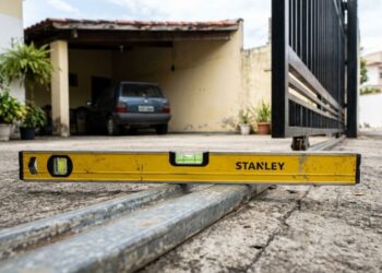 Serralheiro com 22 anos de ofício diz que, em sua experiência, 7 em cada 10 motores de portão automático queimam por causa do desalinhamento do trilho, e mostra a checagem inicial com nível de bolha que o morador pode fazer em cinco minutos, com a alimentação desligada