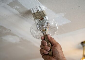 Pintor corta uma embalagem plástica e monta um protetor de pincel que evita respingos ao pintar tetos e paredes altas