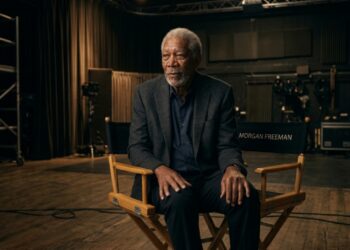 Morgan Freeman sentado em uma cadeira de diretor em um estúdio de cinema, com expressão serena e postura tranquila.