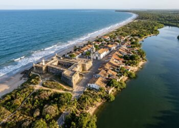 Vista aérea de cidade histórica em uma restinga entre lagoa e oceano, com forte colonial, casario antigo e vegetação costeira. - (Imagem gerada por inteligência artificial-ChatGPT/Olhar Digital)