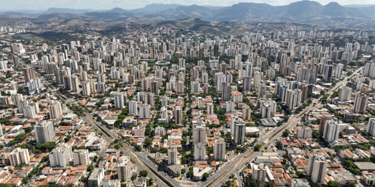 Do alto, Belo Horizonte ainda deixa aparecer a lógica traçada em prancheta no fim do século XIX. Ruas retas formam uma grade, avenidas cruzam o desenho em diagonais e a atual Avenida do Contorno acompanha o limite da zona urbana original. Entre o centro histórico e a Pampulha, a capital mineira transforma planejamento em paisagem cotidiana. Belo Horizonte nasceu de uma planta desenhada em 1895 A planta geral ficou pronta em 23 de março de 1895, quando o engenheiro Aarão Reis a apresentou ao governo mineiro. Segundo a Prefeitura de Belo Horizonte, a zona urbana tinha quarteirões de 120 m por 120 m. As ruas cruzavam-se em ângulos retos, enquanto algumas avenidas cortavam a malha em 45 graus. Porém, a famosa Avenida do Contorno não delimitava toda a área futura da capital. Ela separava a zona urbana planejada da zona suburbana, que seguia outra lógica de ocupação. O plano ainda previa uma zona rural além dessa faixa, reservada a sítios e pequena lavoura. Assim, o desenho visto do alto preserva sobretudo a estrutura central concebida pela Comissão Construtora da Nova Capital no fim do século XIX. 🏛️ 1894: A Comissão Construtora inicia os trabalhos da nova capital.🌿 1895: Aarão Reis conclui a planta geral da cidade planejada.🚀 1897: A nova capital de Minas Gerais é inaugurada em 12 de dezembro. Por que as diagonais cortam o tabuleiro de Belo Horizonte? As diagonais faziam parte de uma solução geométrica deliberada, não de um crescimento improvisado. Aarão Reis combinou ruas ortogonais com avenidas inclinadas, criando cruzamentos que quebravam a regularidade dos quarteirões. Portanto, a vista aérea revela duas ordens sobrepostas na mesma área central. Essa combinação continua fácil de reconhecer quando a malha regular encontra as grandes avenidas. O plano também diferenciava larguras. As ruas receberam 20 m e as avenidas 35 m. Uma grande avenida norte-sul recebeu 50 m. Aarão Reis ainda distribuiu nomes ligados a cidades, rios, montanhas e datas históricas de Minas Gerais e do Brasil. Hoje, caminhar pela região central ajuda a perceber essa lógica nos encontros entre vias retas e diagonais. A geometria não aparece apenas no mapa, ela interfere na orientação, nos cruzamentos e na sequência das quadras. Como enxergar o traçado original durante um passeio? O melhor caminho combina pontos dentro da Contorno com áreas que mostram outras fases urbanísticas da capital. Assim, o visitante percebe a cidade planejada sem transformar o roteiro em uma simples sequência de monumentos. O Parque Municipal nasceu ainda no processo de construção da nova capital, enquanto a Pampulha pertence a outra etapa urbana. Começar no centro e terminar na lagoa evidencia como Belo Horizonte incorporou novas ideias ao longo do século XX. Avenida Afonso Pena: atravessa parte importante da malha original e ajuda a visualizar a diferença entre ruas menores e grandes avenidas do plano. Praça da Liberdade: nasceu ligada ao centro administrativo e conserva a relação entre paisagismo, edifícios públicos e o desenho da nova capital. Parque Municipal Américo Renné Giannetti: inaugurado em 1897, oferece um contraste entre caminhos internos mais livres e a geometria rígida das ruas ao redor. Avenida do Contorno: funciona como referência prática para entender onde terminava a zona urbana prevista no projeto de 1895. Conjunto Moderno da Pampulha: mostra uma etapa posterior, criada em torno da lagoa e inscrita como Patrimônio Mundial em 2016. Quando ir a Belo Horizonte? O inverno costuma reunir os meses mais secos, enquanto o verão concentra os maiores volumes de chuva. Por isso, caminhadas pelo centro pedem atenção ao sol no período seco e à possibilidade de pancadas nos meses mais úmidos. .ant-grid { --cor-primaria: #006E00; /* Verde escuro */ --cor-secundaria: #000000; /* Preto para os destaques */ --cor-txt-secundaria: #B3B3B3; /* Cinza claro para os textos secundários */ display: grid !important; grid-template-columns: repeat(auto-fit, minmax(220px, 1fr)) !important; gap: 20px !important; justify-content: center !important; align-items: stretch !important; padding: 10px !important; margin: 30px auto !important; } .ant-card { border: 2px solid #1a3c1a !important; border-top: 5px solid var(--cor-txt-secundaria) !important; border-radius: 6px !important; background-color: var(--cor-primaria) !important; background-clip: padding-box !important; display: flex !important; flex-direction: column !important; overflow: hidden !important; cursor: pointer !important; box-shadow: 0 6px 16px rgba(0,0,0, 0.2) !important; transition: transform 0.2s ease, box-shadow 0.2s ease, border-color 0.2s ease !important; animation: wmFadeIn 0.6s cubic-bezier(0.2, 0.8, 0.2, 1) backwards; height: auto !important; min-height: 0 !important; margin: 0 !important; padding: 0 !important; } @keyframes wmFadeIn { from { opacity: 0; transform: translateY(30px); } to { opacity: 1; transform: translateY(0); } } .ant-card:hover { transform: translateY(-5px) !important; box-shadow: 0 12px 24px rgba(0, 110, 0, 0.3) !important; border-color: var(--cor-txt-secundaria) !important; } .ant-header { background: #004d00 !important; padding: 18px 10px !important; text-align: center !important; display: flex !important; flex-direction: column !important; align-items: center !important; justify-content: center !important; margin: 0 !important; border-bottom: 1px solid #1a3c1a !important; } .ant-body { background: #ffffff !important; padding: 18px !important; display: flex !important; flex-direction: column !important; flex-grow: 1 !important; align-items: center !important; margin: 0 !important; height: 100% !important; } .ant-card-destaque { border: 2px solid var(--cor-secundaria) !important; border-top: 5px solid var(--cor-secundaria) !important; box-shadow: 0 8px 20px rgba(0, 0, 0, 0.3) !important; } .ant-card-destaque .ant-header { background: var(--cor-secundaria) !important; } .ant-card-destaque .ant-header .ant-titulo { color: #ffffff !important; } .ant-badge-chuva { display: inline-flex !important; align-items: center !important; gap: 5px !important; background: #f0f5f0 !important; color: #555555 !important; font-size: 11px !important; font-weight: 700 !important; padding: 4px 10px !important; border-radius: 4px !important; margin-bottom: 12px !important; text-transform: uppercase !important; letter-spacing: 0.5px !important; border: 1px solid #dcdcdc !important; } .ant-badge-chuva.chuva-alta { background: rgba(204, 17, 17, 0.08) !important; color: #cc1111 !important; border-color: #ffcccc !important; } .ant-badge-chuva.tempo-seco { background: rgba(0, 110, 0, 0.08) !important; color: var(--cor-primaria) !important; border-color: #ccffcc !important; } .pill-ant { display: flex !important; justify-content: center !important; align-items: center !important; text-align: center !important; background: #e6f2e6 !important; color: var(--cor-primaria) !important; font-size: 11px !important; font-weight: 900 !important; letter-spacing: 0.5px !important; padding: 8px 16px !important; border-radius: 4px !important; text-transform: uppercase !important; margin-top: auto !important; margin-bottom: 0 !important; width: 100%; box-sizing: border-box; border: 1px solid #ccdccd !important;} .ant-card-destaque .pill-ant { background: var(--cor-secundaria) !important; color: #ffffff !important; font-weight: 900 !important; border: none !important; } .ant-emoji { font-size: 24px !important; line-height: 1 !important; margin-bottom: 6px !important; display: block !important; } .ant-titulo { color: #ffffff !important; font-size: 16px !important; text-transform: uppercase !important; margin-top: 5px !important; font-weight: bold !important; display: block !important; letter-spacing: 0.5px !important; } .ant-mes { font-size: 11px !important; font-weight: 700 !important; color: var(--cor-primaria) !important; text-transform: uppercase !important; margin-bottom: 8px !important; display: block !important; } .ant-card-destaque .ant-mes { color: var(--cor-txt-secundaria) !important; } .ant-temp { font-size: 20px !important; font-weight: 900 !important; color: var(--cor-primaria) !important; margin-bottom: 8px !important; display: block !important; text-align: center !important; } .ant-card-destaque .ant-temp { color: var(--cor-secundaria) !important; } .ant-desc { font-size: 12px !important; color: #444444 !important; text-align: center !important; line-height: 1.6 !important; margin-bottom: 15px !important; flex-grow: 1 !important; font-family: 'Segoe UI', Roboto, Helvetica, Arial, sans-serif !important; display: block !important;} .ant-desc strong { color: var(--cor-primaria) !important; font-weight: bold !important; } .ant-card-destaque .ant-desc strong { color: #000000 !important; } ☔ Verão Dezembro a Fevereiro 18°C a 27°C 🌧️ 124 a 268 mm/mês O que fazer: Intercalar áreas abertas com museus e espaços cobertos. Atenção: Concentra os maiores volumes de chuva, com frequentes pancadas que exigem um roteiro urbano mais flexível. Status: Estação chuvosa e úmida. ☔ MUSEUS E COBERTOS 🍂 Outono Março a Maio 13°C a 26°C 🌤️ 33 a 149 mm/mês O que fazer: Caminhar pelo centro e pela Praça da Liberdade. Vantagem: O clima começa a estabilizar e as chuvas diminuem significativamente, tornando os passeios muito mais confortáveis. Status: Transição para a época seca. 🍂 CENTRO E PRAÇAS 🌟 Inverno Junho a Agosto 11°C a 24°C ☀️ 6 a 12 mm/mês O que fazer: Explorar trajetos a pé e mirantes urbanos. Dica: É a época mais seca do ano, com sol firme e noites frias. Perfeito para caminhar pela cidade sem medo da chuva. Status: 🌟 Melhor Época! Clima firme e céu limpo. 🌟 TRAJETOS E MIRANTES 🌸 Primavera Setembro a Novembro 15°C a 27°C 🌤️ 49 a 195 mm/mês O que fazer: Combinar passeios pelo centro, parques e o complexo da Pampulha. Atenção: As temperaturas voltam a subir com força, acompanhadas pelo retorno progressivo das pancadas de chuva. Status: Aumento do calor e da instabilidade. 🌸 PARQUES E PAMPULHA As faixas usam mínimas e máximas climatológicas mensais e precipitação média. Consulte a página real do Climatempo antes da viagem. Um desenho que ainda organiza o olhar Belo Horizonte cresceu muito além da malha imaginada no século XIX, mas o centro ainda revela a disciplina geométrica do projeto original. Entre diagonais, quarteirões regulares e a Contorno, a história urbana permanece visível no cotidiano. Essa leitura ganha outra dimensão quando o visitante compara o centro planejado com a paisagem moderna da Pampulha e percebe duas épocas urbanísticas. Na próxima visita, escolha um ponto alto ou caminhe pelo centro e tente reconhecer esse tabuleiro por conta própria, mesmo sem mapa. Leia mais: Steve Jobs, “Seu tempo é limitado”, por que perceber que a vida acaba pode mudar a maneira como escolhemos vivê-la Por que cidades cada vez mais quentes estão clareando os telhados das casas, e o efeito não termina dentro dos imóveis Psicólogos investigam por que algumas pessoas estão cansadas, querem dormir, mas continuam adiando a hora de ir para a cama, estudos recentes tratam a chamada procrastinação do sono como problema de autorregulação