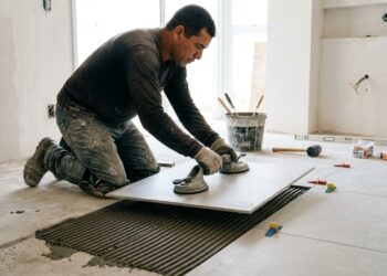 Pedreiro posicionando uma grande placa de porcelanato cinza com ventosas sobre contrapiso preparado com argamassa, ao lado de peças já instaladas. (Imagem gerada por inteligência artificial-ChatGPT/Olhar Digital)