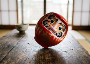 Boneco Daruma japonês vermelho sobre uma mesa de madeira, símbolo associado à perseverança e à capacidade de se reerguer. - (Imagem gerada por inteligência artificial-ChatGPT/Olhar Digital)
