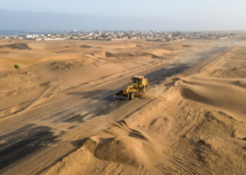 A cidade construída diante de um campo de dunas onde a areia atravessa estradas durante determinados períodos do ano e máquinas precisam abrir caminho novamente