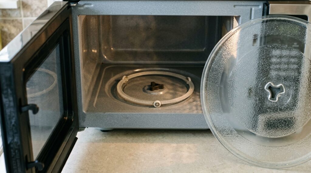 Interior de micro-ondas sem o prato de vidro, exibindo o anel plástico com roletes e o acoplador central responsáveis pela rotação. - (Imagem gerada por inteligência artificial-ChatGPT/Olhar Digital)