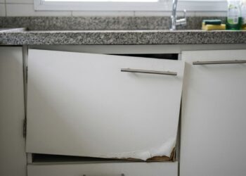 Armário planejado de MDF branco com porta desalinhada e borda inferior inchada pela umidade em cozinha residencial. - (Imagem gerada por inteligência artificial-ChatGPT/Olhar Digital)