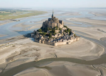 Vista do alto, uma vila medieval francesa parece surgir no meio do mar, mas a paisagem muda completamente quando a maré recua e revela enormes bancos de areia