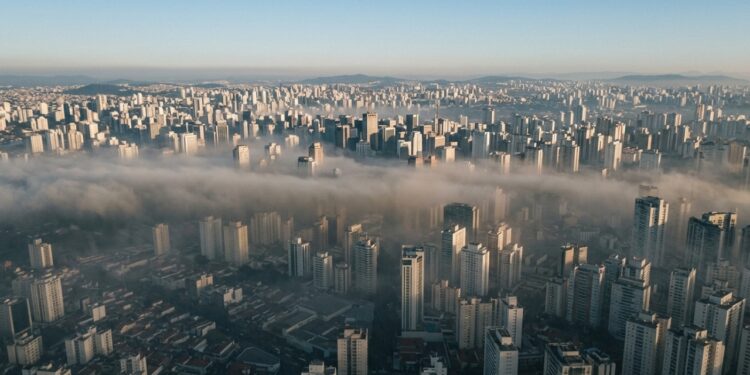 Vista aérea de São Paulo com prédios parcialmente encobertos por uma camada espessa de poluição acinzentada durante uma manhã de inverno, ilustrando os efeitos da inversão térmica. - (Imagem gerada por inteligência artificial-ChatGPT/Olhar Digital)