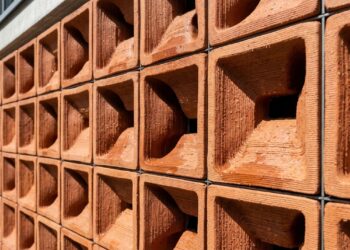 Parede de módulos cerâmicos terracota impressos em 3D, com canais curvos e superfície úmida, instalada em fachada moderna. - (Imagem gerada por inteligência artificial-ChatGPT/Olhar Digital)