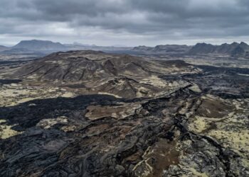 Vista aérea de terreno vulcânico escuro na Islândia, com elevação suave e fissuras antigas em meio a campos de lava solidificada. - (Imagem gerada por inteligência artificial-ChatGPT/Olhar Digital)
