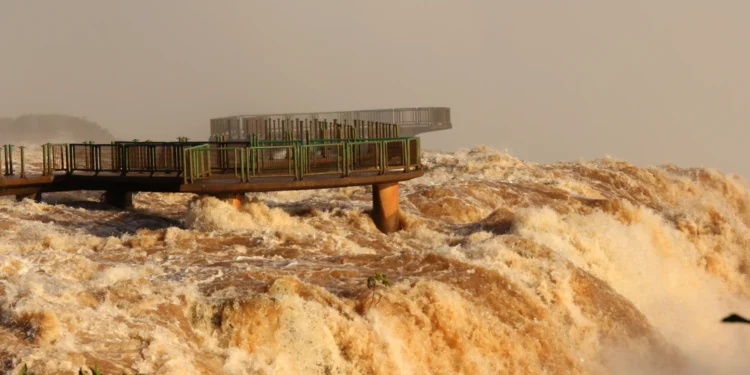 Fotografia histórica de junho de 2013 mostra água barrenta em grande volume passando sob e ao redor da passarela vazia das Cataratas do Iguaçu.