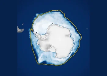 Mapa da NASA visto de cima do polo sul: o continente antártico em branco, cercado por um anel de gelo marinho branco-azulado sobre o oceano azul-escuro, com uma linha amarela marcando a extensão mediana histórica do gelo.