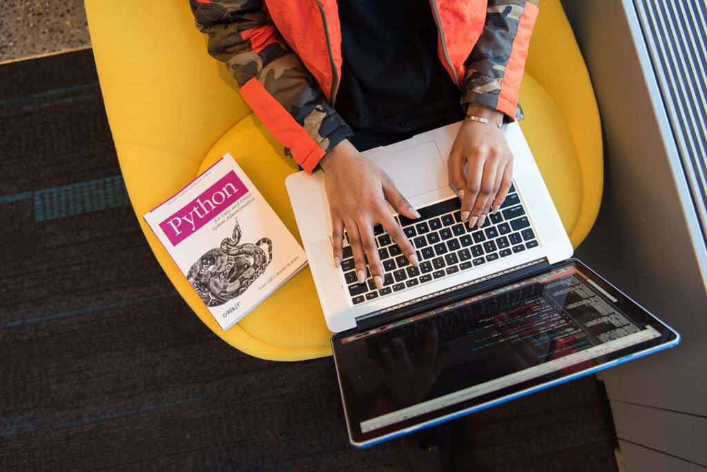 mulher programando em notebook ao lado de livro sobre python
