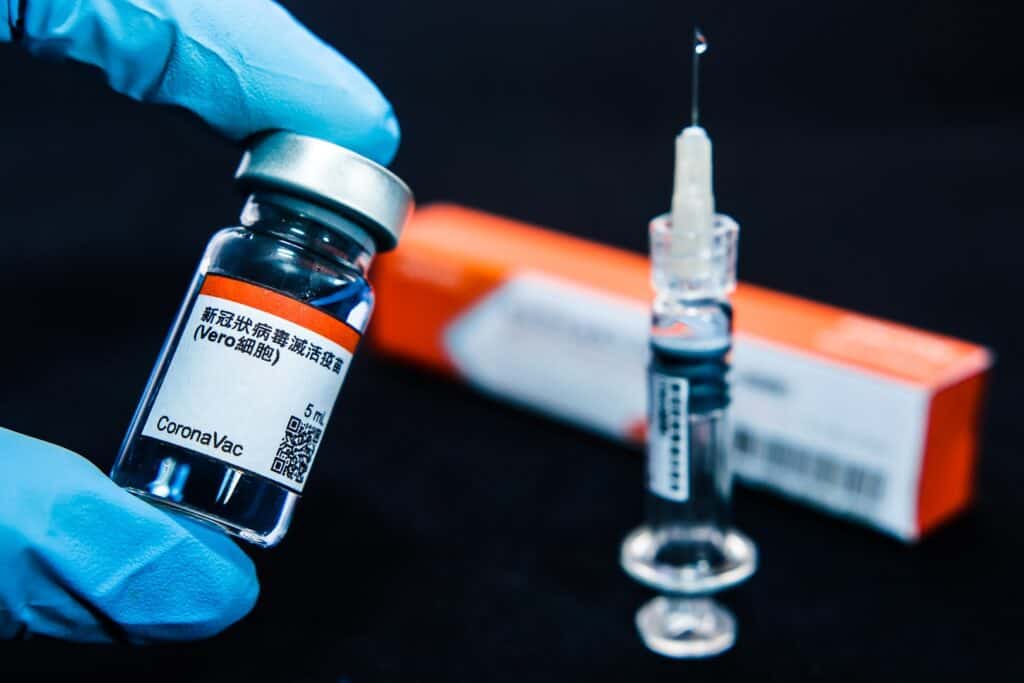 Seringa borrada, um pacote e uma mão com luvas azuis e segurando uma dose da vacina contra a COVID-19, a Coronavac