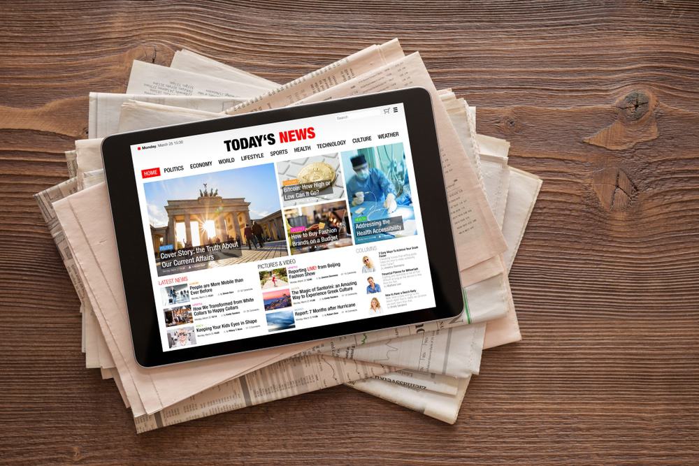Tablet com site de notícias aberto, em cima de pilha de jornais