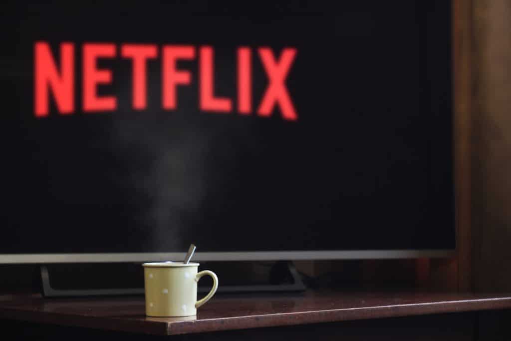 Imagem mostrando um televisor exibindo a logomarca da Netflix ao fundo, com uma xícara de café à frente