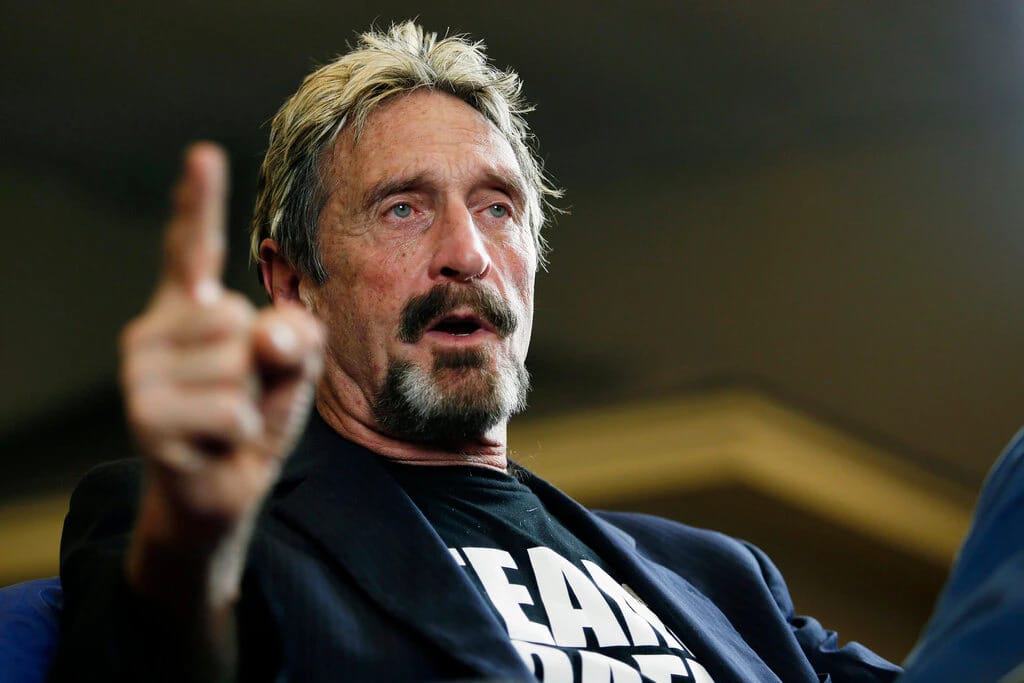Imagem mostra John McAfee, ex-empresário da tecnologia, durante palestra, vestindo paletó com o dedo em riste