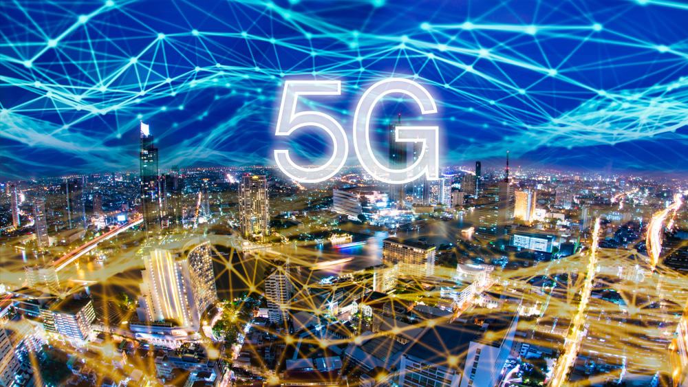 Cidade ilustrada à noite. Por cima há uma rede de luz, como se fosse uma rede de conexão à Iinternet, com o texto 5G por cima.