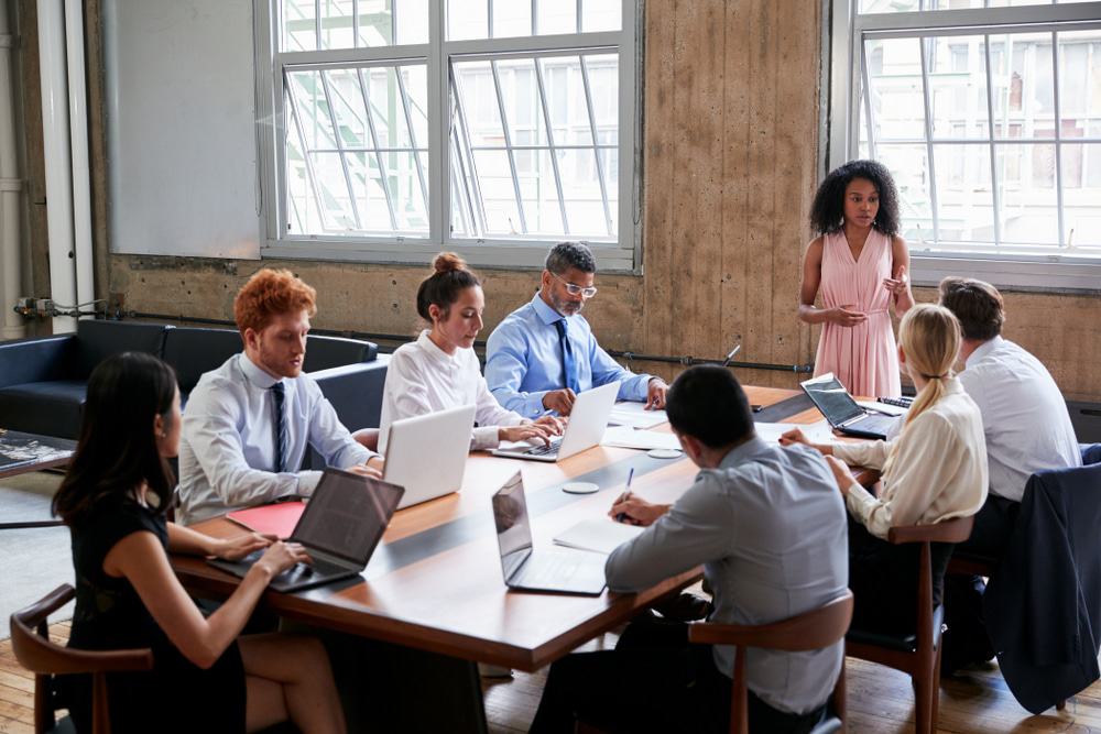 Equipe liderada por uma mulher, em volta de uma mesa de reunião