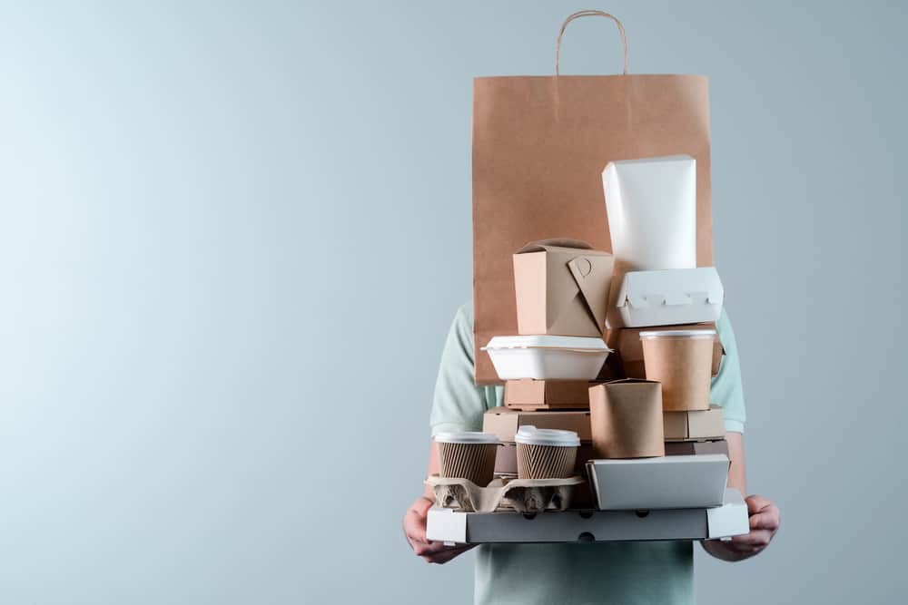 Imagem mostra uma pessoa carregando várias embalagens de delivery de comida.