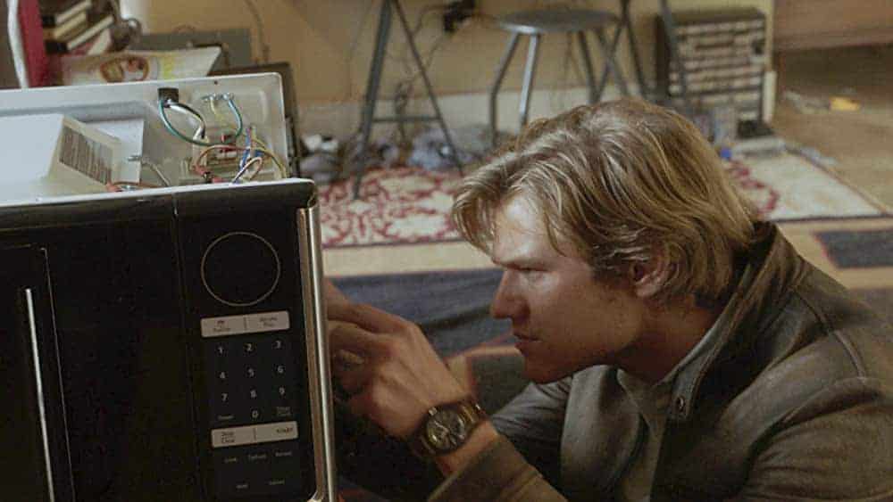 Imagem mostra o ator Lucas Till no papel de Angus MacGyver, mexendo nos fios de um microondas aberto