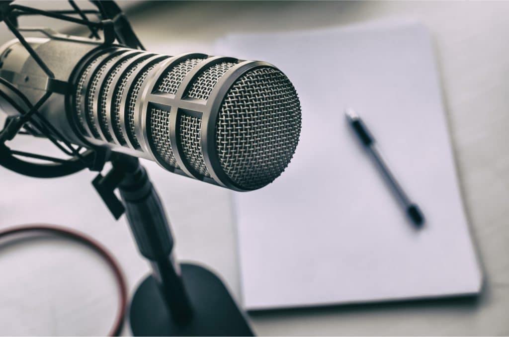 Spotify lança plataforma de assinatura para podcasts, competindo com a Apple. Na imagem: um microfone de podcast, com uma caneta e papel de anotações ao fundo