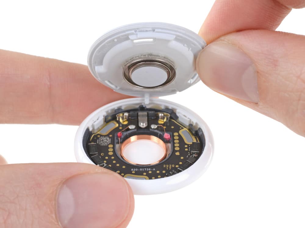 Uma AirTag aberta. O alto-falante está na metade de cima, a placa de circuito na debaixo. Imagem: iFixIt