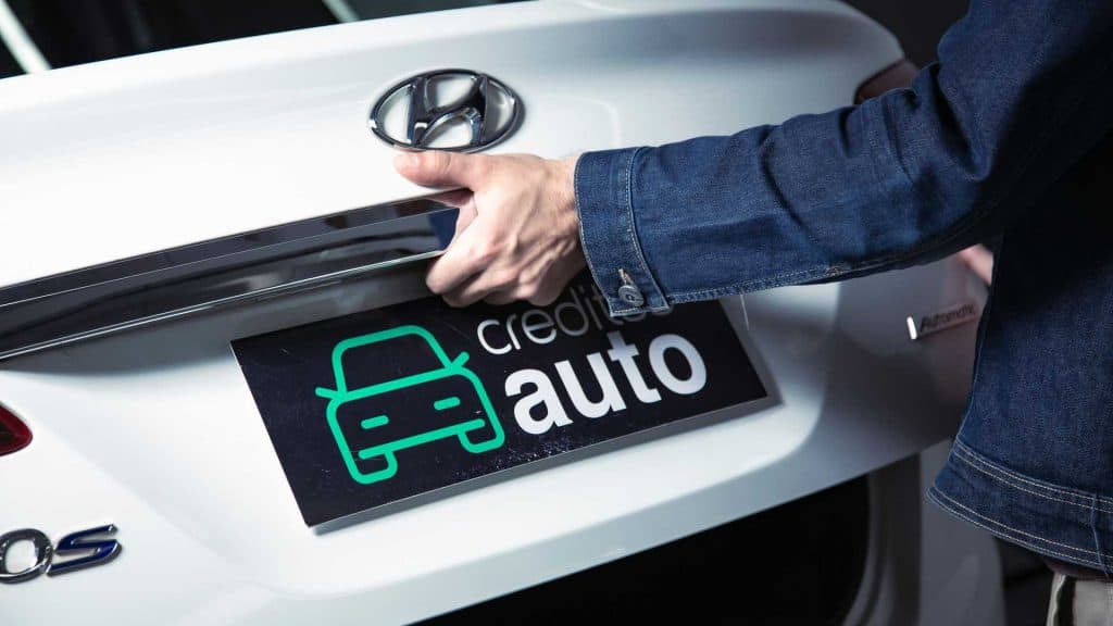 Porta-malas de um carro branco sendo aberto por um homem de camisa jeans