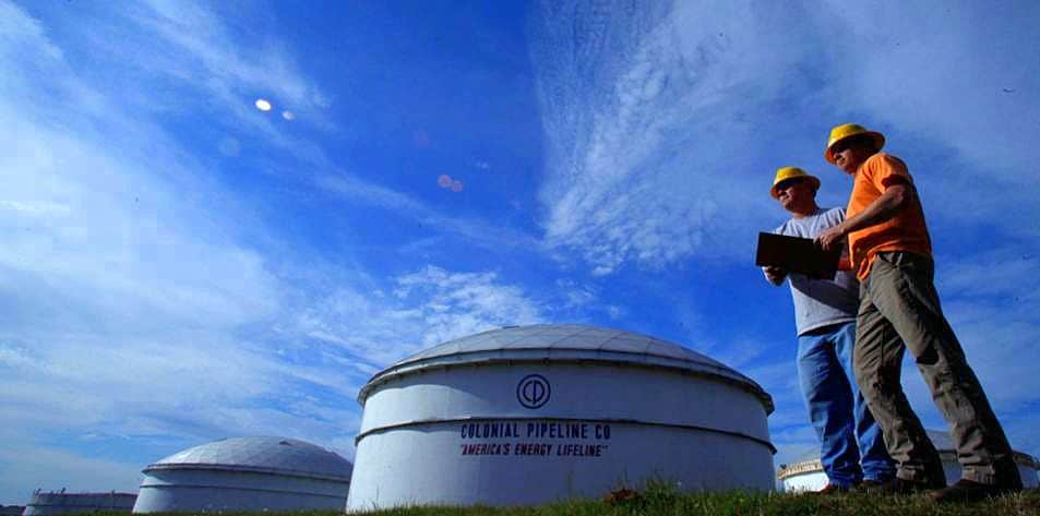 Imagem mostra dois homens ao lado de um duto da Colonial Pipeline