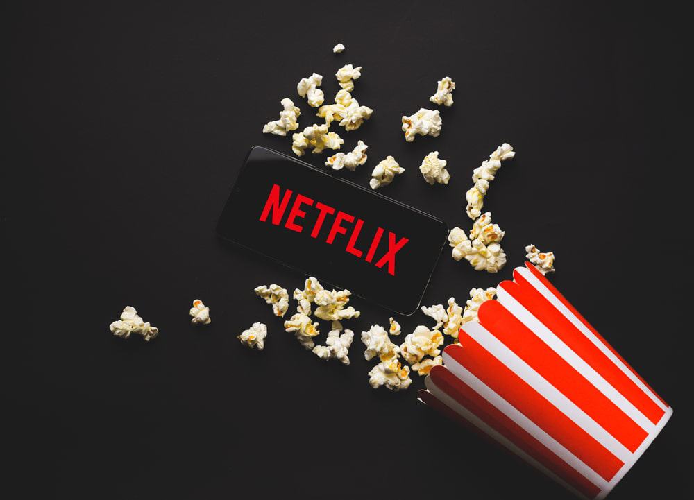 Logo da Netflix em um celular junto com um pote de pipoca