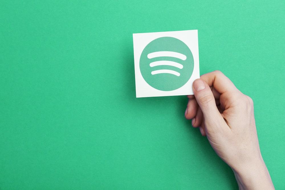 Imagem de fundo verde mostra uma mão segurando um cartão com o logotipo do Spotify