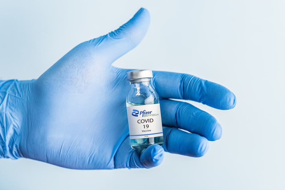 Mão de luva azul segurando um frasco de vidro da vacina da Pfizer contra a Covid-19