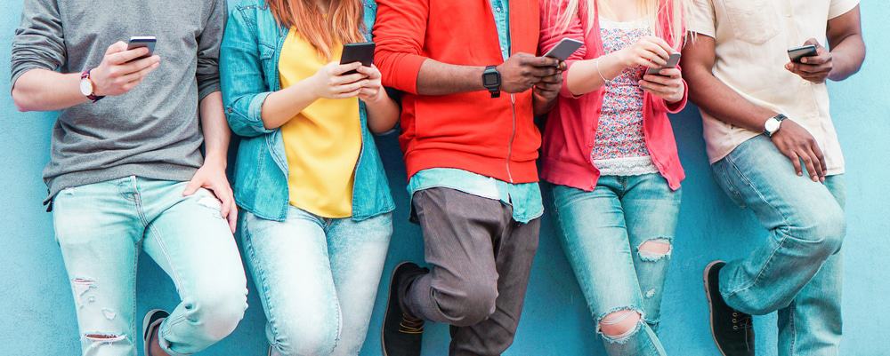 Imagem mostra corpos jovens, todos utilizando smartphones