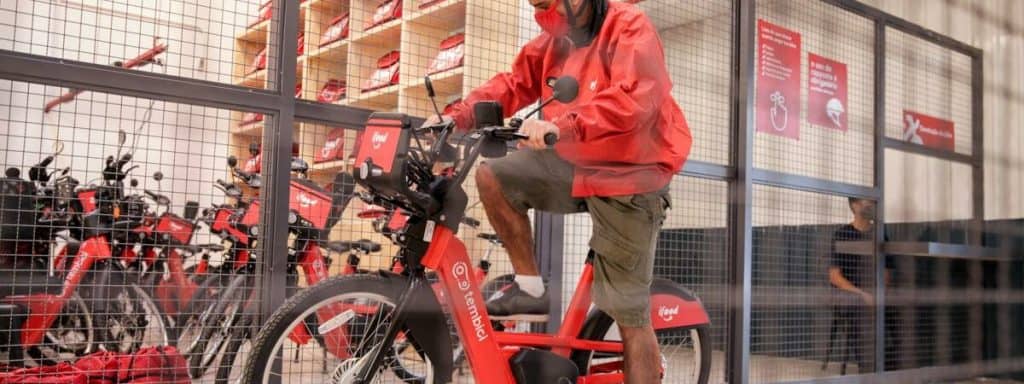 Imagem mostra um entregador uniformizado, montando uma bicicleta elétrica da Tembici em parceria com o iFood