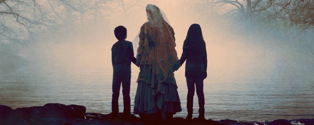 Imagem promocional do filme mostra Chorona segurando pelas mãos duas crianças, uma de cada lado, de frente para um lago.
