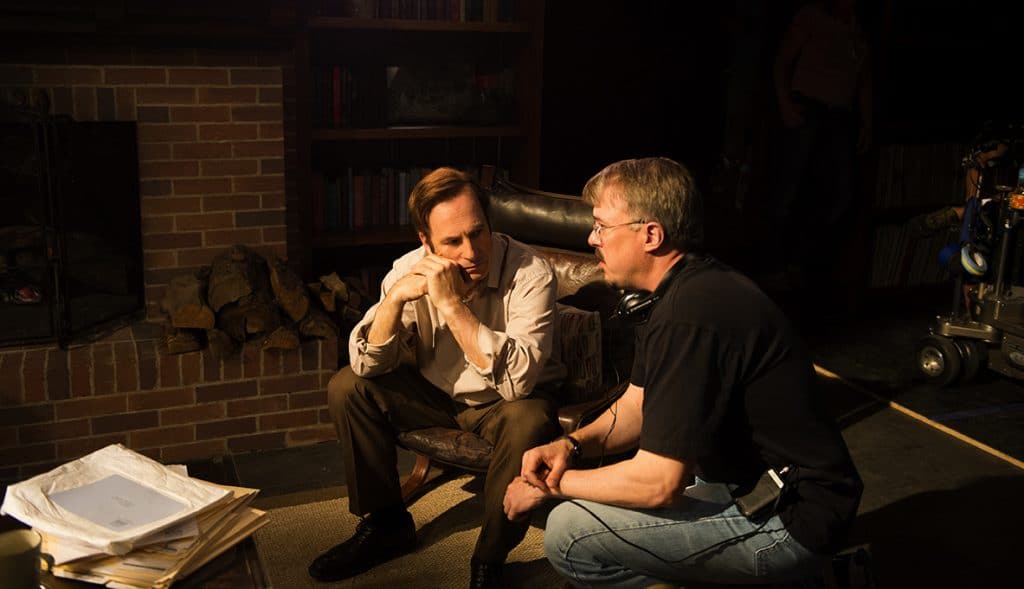 Bob Odenkirk conversa com Vince Gilligan em set de 'Better Call Saul'. Os dois podem ser vistos em uma sala escura, e o ator parece receber instruções do diretor. 