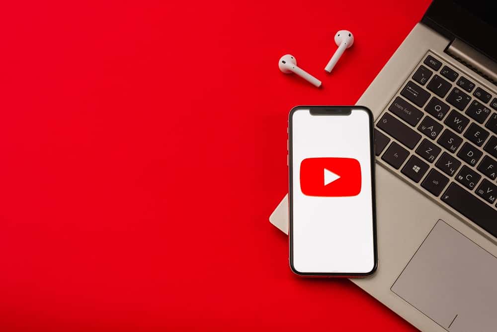 Imagem mostra logo do youtube na tela de um smartphone que, por dua vez, encontra-se em cima de um teclado de notebook. O fundo da imagem é vermelho