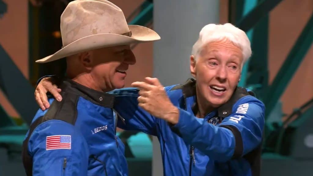 Imagem mostra Jeff Bezos, vestindo roupa de astronauta e um chapéu de caubói, abraçando Wally Funk, a pessoa mais velha a ir para o espaço, durante coletiva de imprensa da Blue Origin