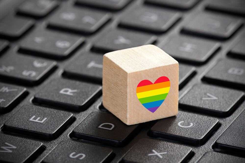 Imagem mostra um cubo de madeira com um coração nas cores do arco-íris colocado em cima de um teclado de notebook