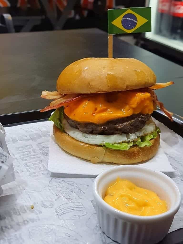 Foto mostra um hambúrguer artesanal, com molho à frente, em cima de uma bandeja