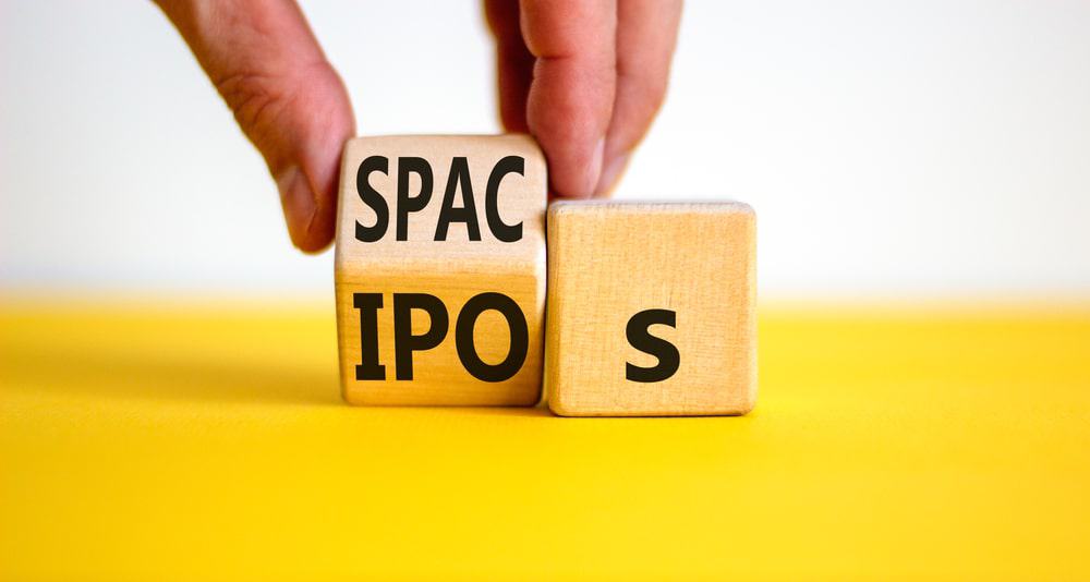 Mãos segurando dados de madeira com as escritas SPACs e IPOs