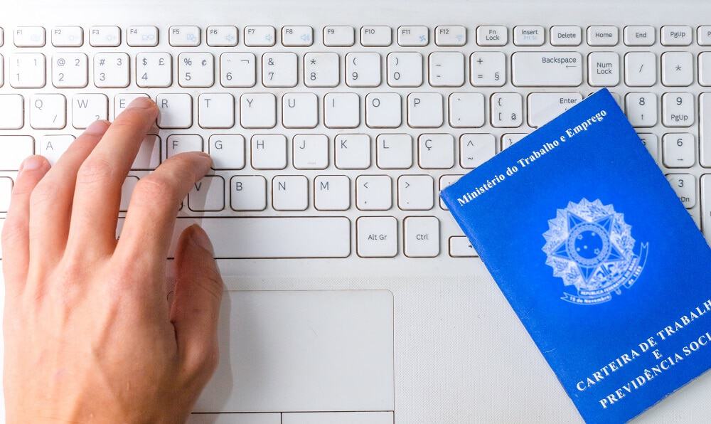 mão em cima do teclado com carteira de trabalho ao lado