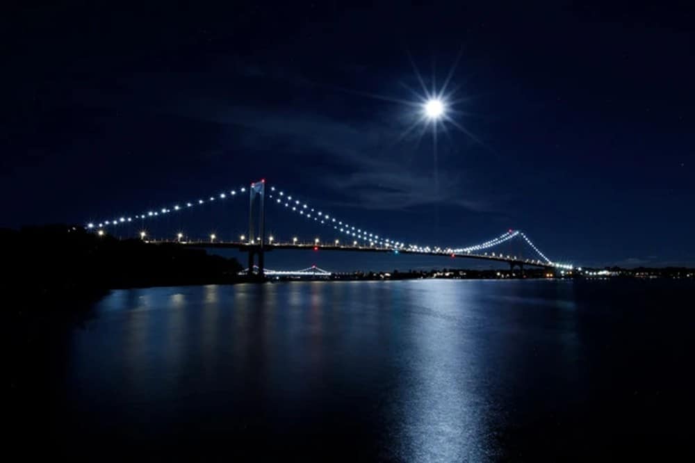 Foto da Ilha da Colheita se mostrando no alto, por trás de uma ponte em área urbana
