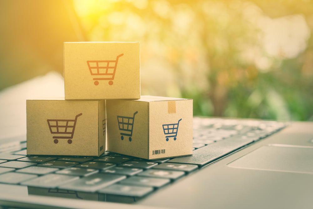 Conceito de comércio eletrônico com caixas e um carrinho de compras em um teclado de laptop. Imagem ilustra clientes encomendando produtos de sites de varejistas através da internet.