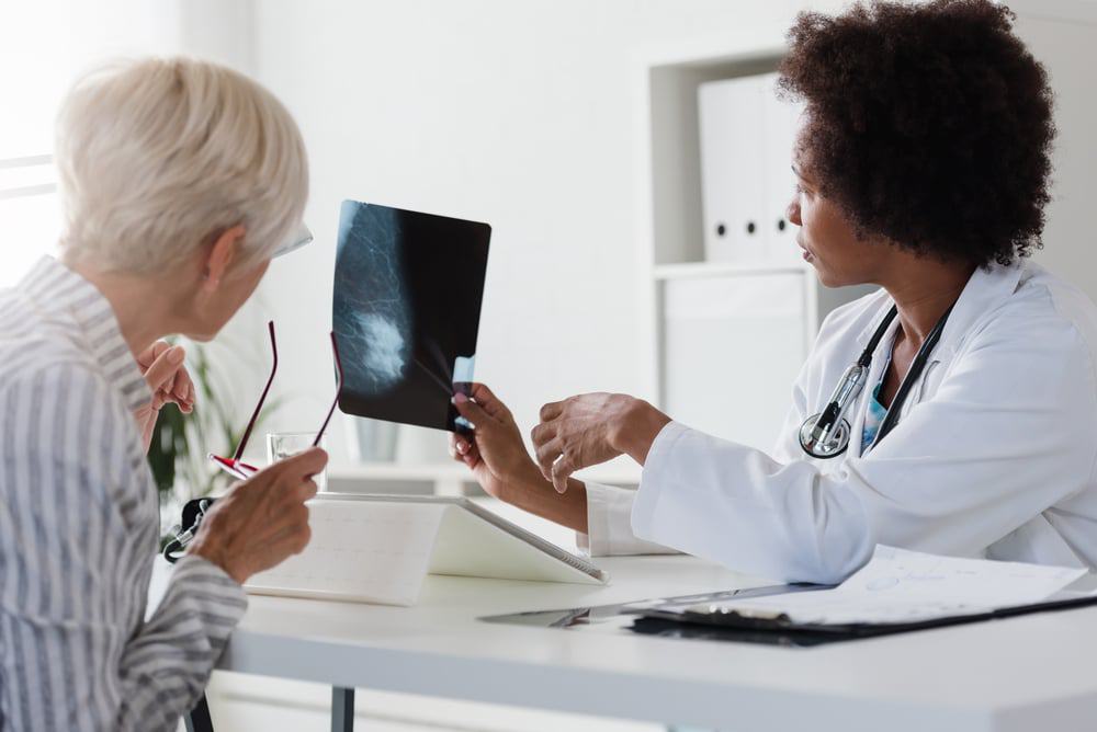 Imagem mostra duas mulheres, uma médica e outra paciente, analisando exame de câncer de mama