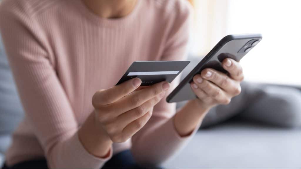 Mulher segura cartão de crédito em uma mão e celular na outra