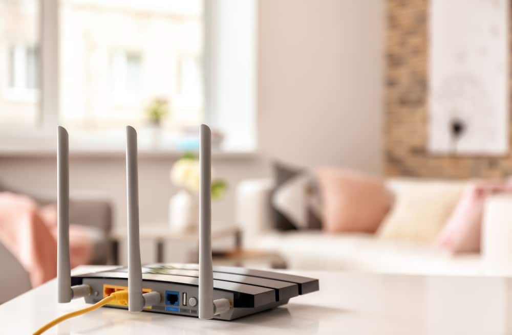 Roteador Wi-Fi posicionado em cima de uma bancada com sofás ao fundo 
