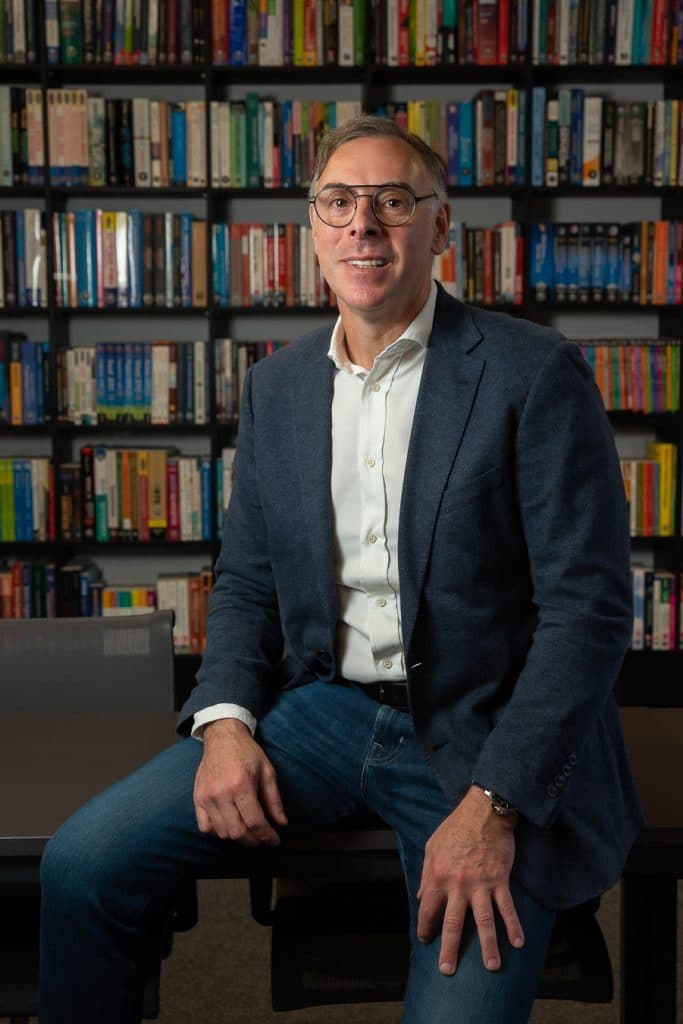 Celso Kiperman, CEO da +A Educação, sentado; ao fundo uma parede feita de estante com livros