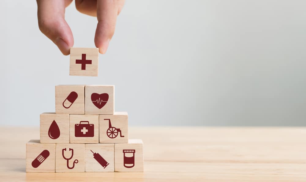 Mão organizando e empilhando blocos de madeira com ícones de assistência médica e plano de saúde; conceito de saúde.
