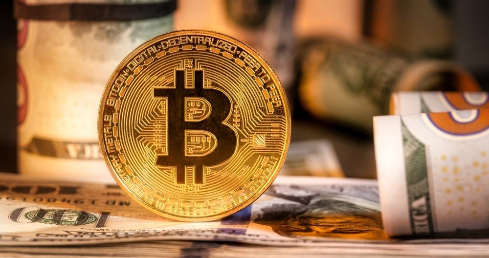 Iluistração de uma moeda de bitcoin com notas de dólar americano ao fundo.